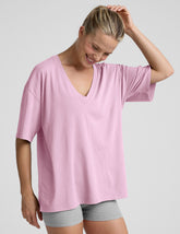 model wearing a pink oversized v-neck top and gray shorts on a plain background.